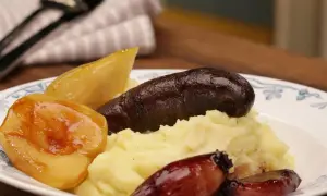 Herzhaftes Gericht mit Kartoffelpüree, dunkler Wurst, karamellisierten Zwiebeln und Birnenstücken – eine köstliche Kombination aus Himmel und Erde.