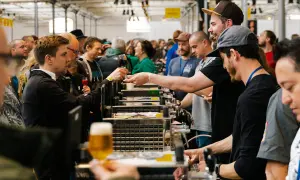 Folla a un evento di degustazione di birra a Mikkeller Copenhagen. Un uomo porge un bicchiere di birra scura.