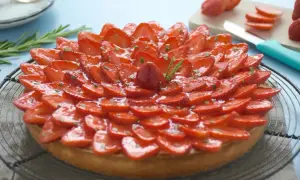 Tarte fraise aux fraises fraîches, joliment disposées en rosace sur une pâte dorée, garnie de quelques brins de romarin.