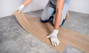 Manos enguantadas colocando una tabla de suelo vinílico sobre un suelo de hormigón.