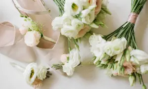 Eleganckie, jasnoróżowe buty ślubne z małymi białymi kwiatami w bukietach i butonierkach.