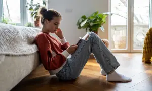 En flicka sitter på golvet, försjunken i sin telefon. Hennes hållning och ansiktsuttryck kan antyda depression hos barn.