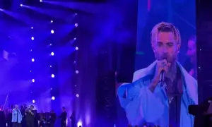 Quebonafide koncert na żywo. Artysta śpiewa do mikrofonu, a jego twarz widać na wielkim ekranie. Tłum szaleje.