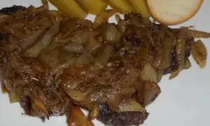 Pyszna kaszanka z patelni, duszona z cebulką, podana z ogórkiem kiszonym i kromką chleba.