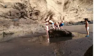 Un grupo de niños exploran una poza en la playa, rodeados de acantilados rocosos.