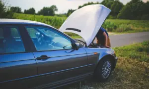 Samochód z otwartą maską na poboczu drogi. Kierowca pochyla się nad silnikiem, być może zmagając się ze **spalaniem stukowym**.