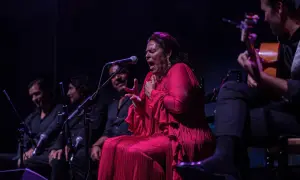 Una cantante colombiana flamenco, con un vestido rojo vibrante, canta apasionadamente acompañada por guitarristas.