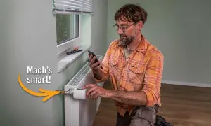 Mann mit Smartphone installiert smarten Thermostat an Heizkörper. Einfach das Thermostat wechseln und Energie sparen.