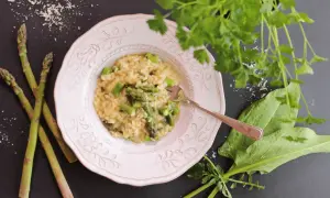 Un crémeux risotto asperges, garni de morceaux d'asperges fraîches, servi dans une assiette rose, avec des asperges crues à côté.