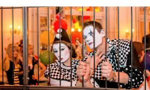 Zwei Clowns hinter Gittern, bereit für den Dresden Karneval. Bunte Ballons und Lichter im Hintergrund.