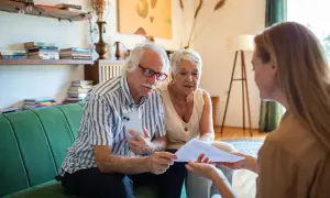 Un couple âgé discute avec une conseillère des modalités de calcul du paiement d'une maison de retraite par les descendants.
