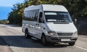 Weißer Kleinbus von Polen nach Deutschland fährt auf einer Straße durch eine hügelige Landschaft.