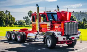Un impressionnant Kenworth, un camion américain rouge vif, brille sous le soleil. Ses chromes étincelants et ses échappements imposants annoncent sa puissance.