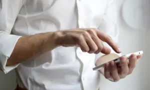 Mężczyzna w białej koszuli sprawdza stan konta w Plusie na swoim smartfonie.