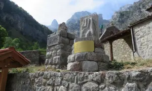 Monumento en piedra con inscripciones y un relieve, con montañas al fondo. El cartel dice "EL CAIN DE ARRIBA".
