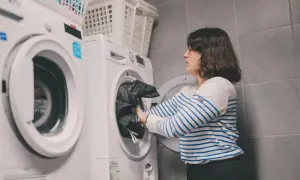 Kobieta wkłada czarne ubrania do pralki. W tle suszarka i kosze na pranie. Tak właśnie pracuje polar.