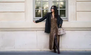 Elegancka kobieta w sukience w panterkę i czarnym blazerze, z beżową torebką i brązowymi kozakami dla niskiej osoby, które optycznie wydłużają nogi.