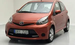 En orange Toyota Aygo med registreringsskylten DRY 720. Bilen verkar ha ett problem med fronten, kanske en buckla eller skada.