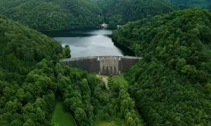 Zapora w górach Dolnego Śląska, otoczona gęstym, zielonym lasem. Woda w zbiorniku odbija pochmurne niebo.
