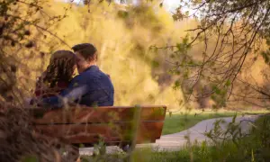 Pareja abrazada en un banco, compartiendo un momento de amor verdadero entre la naturaleza.