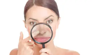 Donna esamina il suo naso con una lente d'ingrandimento, concentrandosi su un punto nero incistato.