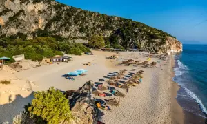 Piękna plaża w Albanii, morze lśni w słońcu, a klif tworzy malownicze tło dla leżaków i parasoli.
