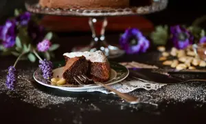 Ein Stück saftiger italienischer Schokokuchen, bestäubt mit Puderzucker, auf einem Teller mit Mandeln und lila Blumen.