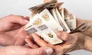 Dwie pary rąk przekazują sobie plik banknotów 200 zł. Może to być darowizna, od której należy zapłacić podatek od darowizny.