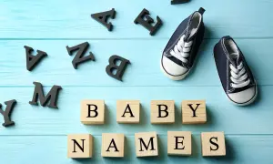 Des lettres noires forment "BABY NAMES" sur des cubes en bois. Une paire de chaussons bleus attend. Quel joli prénom en M pour le bébé ?