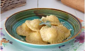 Tortelli di patate fumanti, cosparsi di parmigiano e guarniti con salvia, in una ciotola colorata.