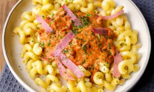 Gedrehte Nudeln mit cremiger Tomatensoße und rosa Wurststreifen, garniert mit Petersilie.