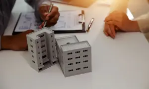 Dwie osoby omawiają plany dotyczące przepisania mieszkania na dziecko. Na stole modele budynków.