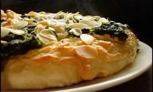 Eine köstliche Spinat Pizza mit knusprigem Teig und gerösteten Mandelblättchen. Dampf steigt auf und verspricht ein warmes, herzhaftes Gericht.