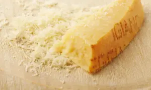 Ein Stück Parmesan mit geriebenem Käse auf einem Holzbrett.