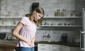 Kobieta w kuchni trzyma się za brzuch, odczuwając pulsowanie. Może to być objaw nerwicy.