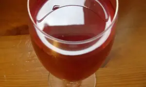 Czerwone wino z róży w kieliszku, na drewnianym stole. Delikatny, rubinowy kolor napoju.
