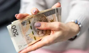 Dłonie trzymające stos banknotów 200 zł. Zastanawiasz się, jak wypłacić pieniądze z PPK?