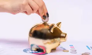Dłoń wrzuca monetę do złotej świnki-skarbonki. Kredytobiorca oszczędza na przyszłość, budując finansową poduszkę.