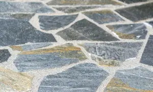 Nahaufnahme von polygonalplatten verlegen. Die unregelmäßigen Steine sind grau und gelblich, mit hellem Sand dazwischen.