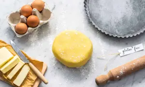Impasto giallo per pasta frolla senza glutine, uova, burro e stampo per crostata pronti per creare un dolce delizioso.