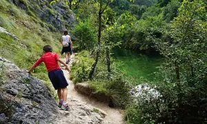 Niños exploran la senda de la hoya de san vicente, junto a un río de aguas cristalinas y vegetación exuberante.