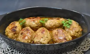 Roladki z mięsa mielonego z piekarnika, soczyste i rumiane, w sosie, ozdobione natką pietruszki.