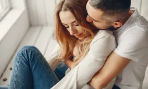 Mężczyzna obejmuje kobietę, szepcząc jej do ucha. To prawdziwe bombardowanie miłością, czułe i intymne.