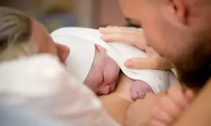Pierwsze chwile po narodzinach. Noworodek otulony kocykiem, rodzice z czułością dotykają maleńkiego ciałka. Tak wygląda poród.