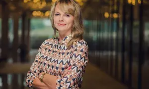 Portret uśmiechniętej kobiety w kolorowej bluzce, z rękami skrzyżowanymi na piersi.