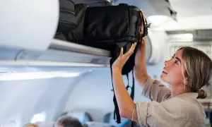 Junge Frau verstaut ihren großen Backpacking Rucksack im Gepäckfach eines Flugzeugs.
