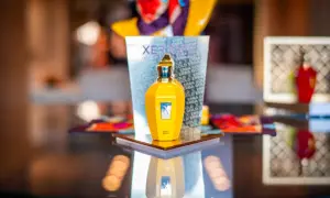 Żółta butelka perfum Xerjoff Erba Gold na lustrzanym blacie, odbijająca się w tafli.