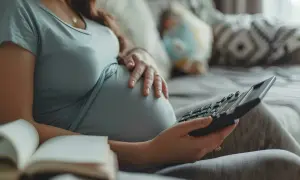 Ciężarna kobieta z kalkulatorem i otwartą książką na kanapie.