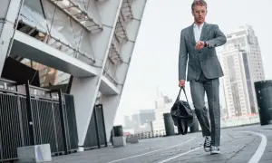 Mężczyzna w garniturze i trampkach do garnituru idzie z torbą obok nowoczesnego stadionu.