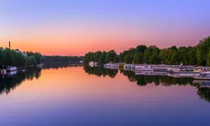 Boote liegen im Wasser vor dem grünen Ufer des Treptower Parks im Abendrot.